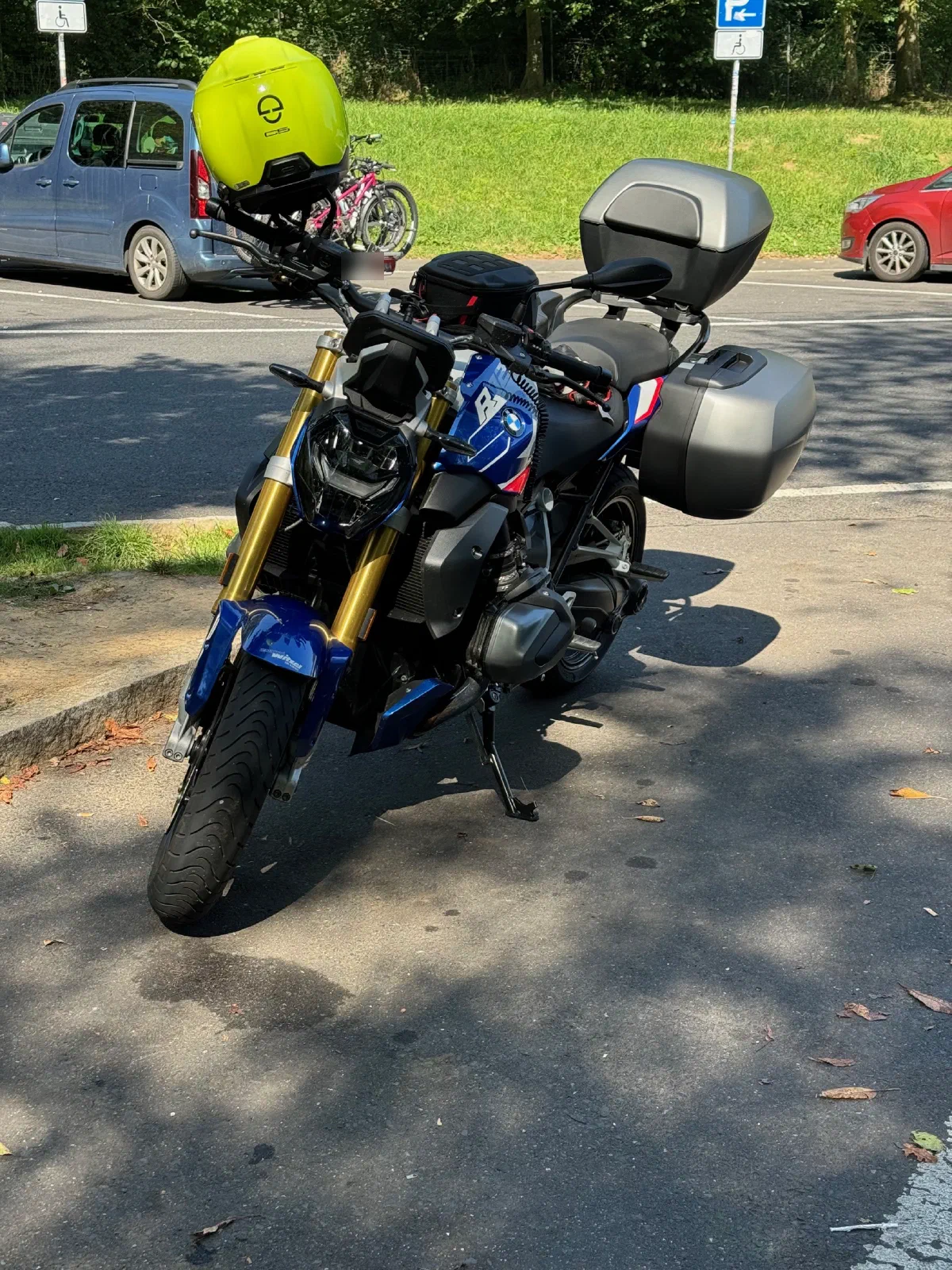 A BMW R 1250 R with side cases and a top case in a parking lot, the helmet hanging from the mirror