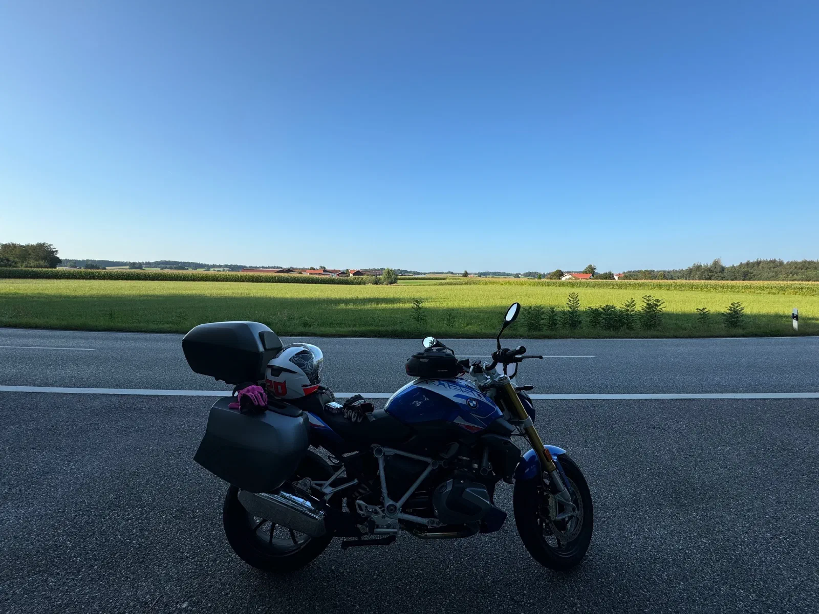 The loaded motorcycle at the edge of a country road, fields behind it